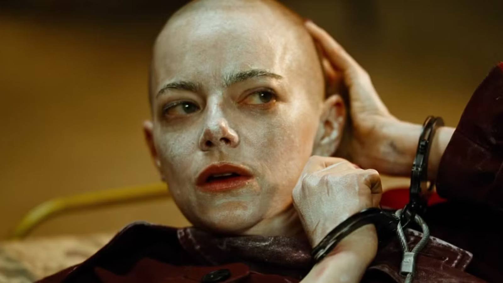 Emma Stone handcuffed and touching her bald head in Bugonia