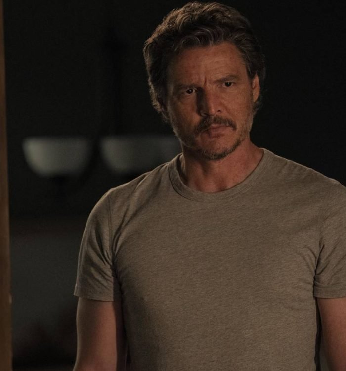 Pedro Pascal as Joel Miller in The Last of Us looking ahead curiously while standing in a doorway